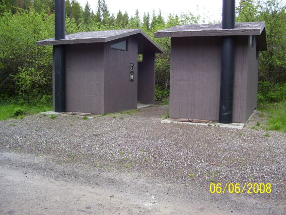 picture showing Two accessible, unisex, bathrooms and an 8-foot, 5 degree slope between the campground road and the bathroom entrance ways.  A 1.5-inch step between the gravel access route and the concrete bathroom floor can be seen.