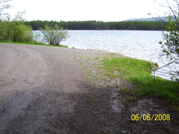 picture showing View of the short, steep boat launch from the campground road.  Part of the lake can be seen in the background.  The small amount of shoreline (about 30 feet) is the only open shoreline available at the campground without bushwhacking through vegetation and soft loose ground between campsites and the lake.