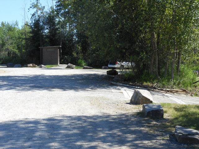 picture showing Gravel parking lot with latrine in the background.