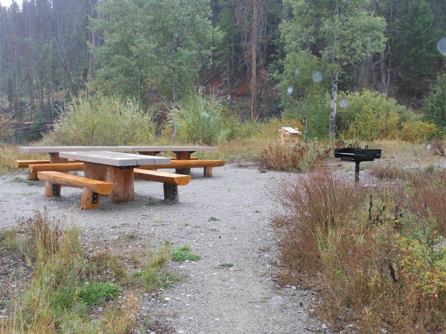 picture showing At the Lower Eagle Nest site, a small grouping of 3 accessible tables with fire grill.  The gravel trail from the parking lot is somewhat rough.