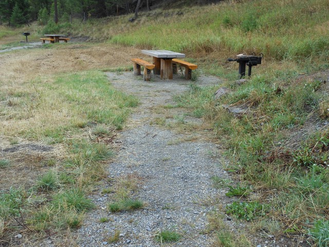 picture showing Table and grill at the north end access site of the park.  The gravel trail is somewhat rough because of the vegetation in the trail tread way.