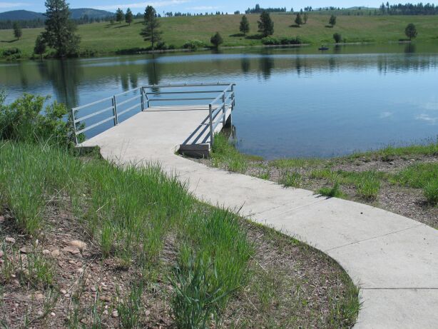 picture showing Paved access route leading from the paved marked accessible parking space down to a paved fixed dock with side guardrails and fixed fishing pole holders.