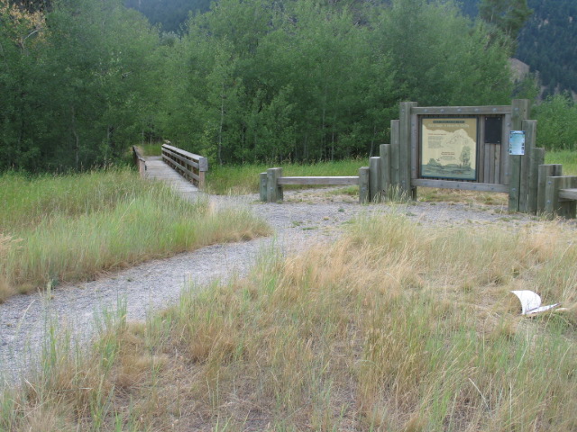 picture showing Trailhead showing a wide gravel path and an informational sign in the background.