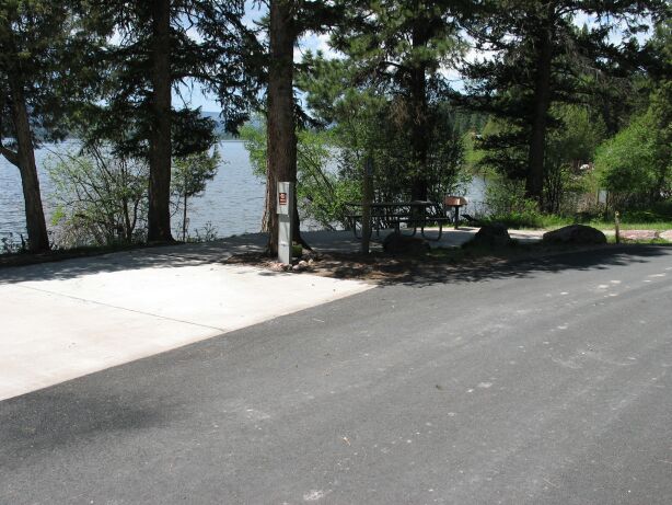 picture showing Accessible campsite (campsite number 16) showing paved parking pad and paved access route to a wheelchair-friendly picnic table and BBQ stand, and electric hookup.  The paved path can be seen continuing on toward the boat launch area.  This picture also shows the excellent view of the lake.