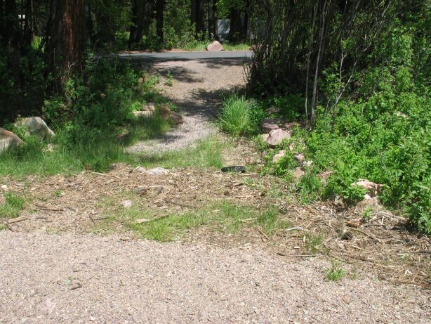 picture showing The inaccessible route from the campground road down to the dedicated swimming area.  The route is steep, narrow, and unstable, and has large rocks creating high tread obstacles.  A wide section of small driftwood derbies must also be crossed before reaching the small gravel beach.