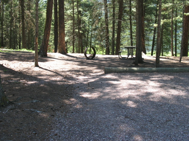 picture showing Example of several other campsites in the campground showing a packed dirt campsite with uneven ground and a slightly raised gravel parking pad.  The uneven ground, while smooth, may create slope and cross slope hazards.  There may also be tread obstacles from roots.  The BBQ cooking surface is lower than 15 inches.