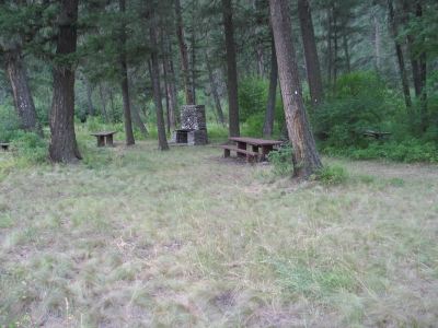picture showing Picnic area showing the stone cooking structure and several picnic tables.  There is uneven ground in the foreground of the picture, which must be crossed to access the picnic area.